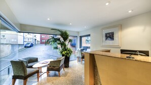 Een hotel lobby met een receptiebalie, een zithoek en grote ramen met uitzicht op de straat.