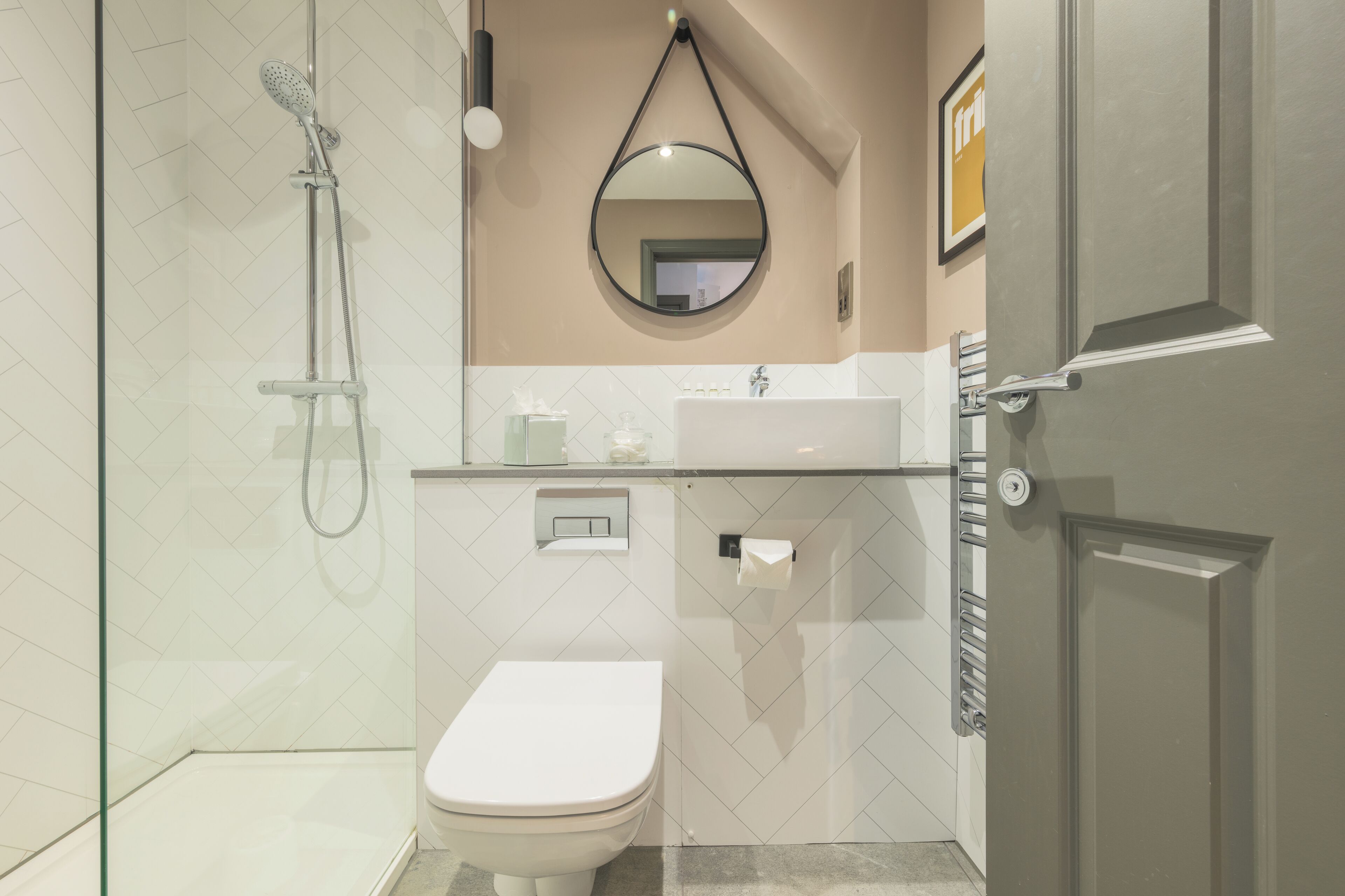 Ein modernes Badezimmer mit einer Duschkabine, einer weißen Toilette, einem Waschbecken mit Spiegel darüber und einer Tür rechts.