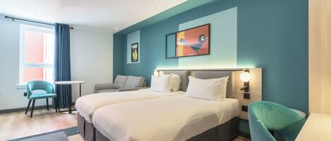 Una habitación de hotel con dos camas, una mesita pequeña, una silla y un ventanal con cortinas.