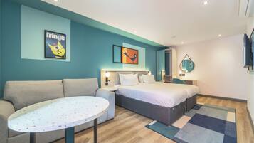 A modern hotel room with a sofa, a bed, a round table, and artwork on the walls.