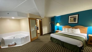 A hotel room with a large bathtub, a bed with a green bedspread, a wooden headboard, and a blue accent wall. - American Inn and Suites (Peosta)