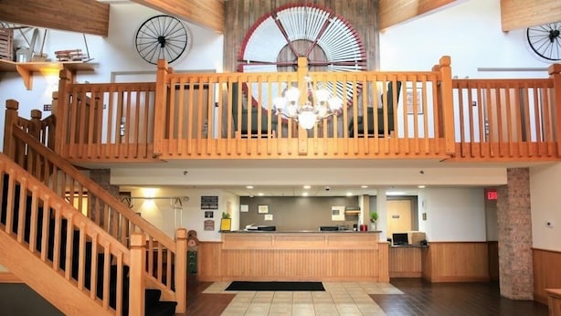 A hotel lobby with a wooden reception desk, a staircase, and a large fan on the ceiling. - American Inn and Suites (Peosta)
