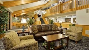 A spacious lobby with a high ceiling, a staircase, and a seating area with a sofa and armchairs. - American Inn and Suites (Peosta)