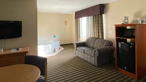A hotel room with a television, a striped sofa, a dining table, a microwave, and a coffee maker. - American Inn and Suites (Peosta)
