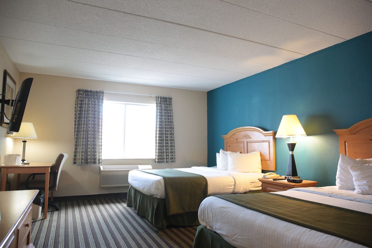 A hotel room with two beds, a desk, a chair, a TV, and a window with curtains.