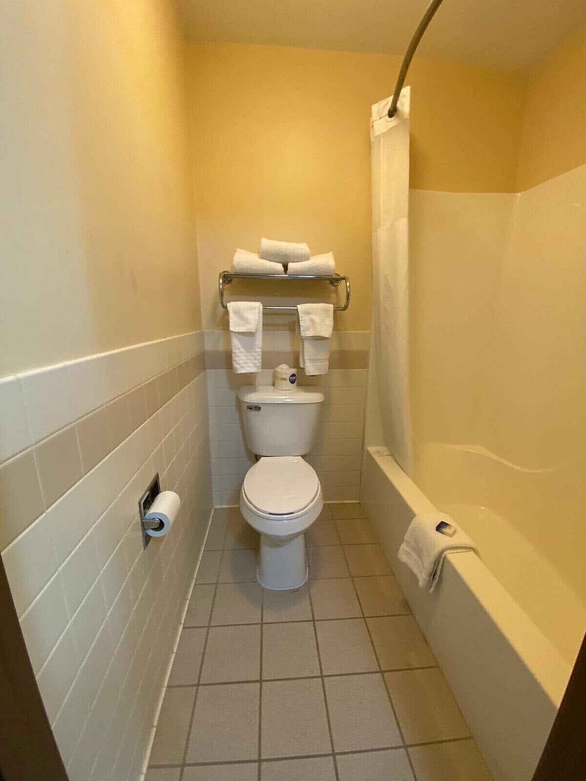 Un baño pequeño con inodoro, toallero con toallas, dispensador de papel higiénico y bañera.