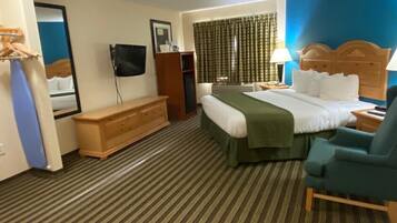 A hotel room with a bed, a desk, a chair, a dresser, a television, and a window with curtains.