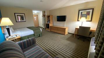 Habitación de hotel con cama, sofá a rayas, escritorio con silla, televisor y lámpara.