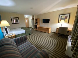 Habitación de hotel con cama, sofá a rayas, escritorio con silla, televisor y lámpara.