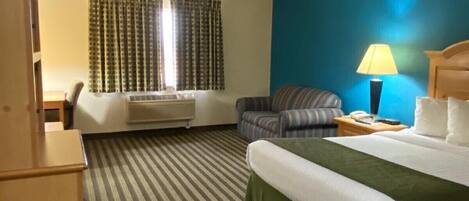 Habitación de hotel con cama, silla, escritorio, lámpara y ventana con cortinas.