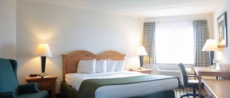 A hotel room with a bed, two bedside tables with lamps, a desk, a chair, and a window with curtains.