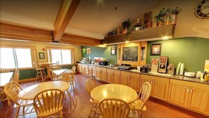 A spacious kitchen with wooden cabinets, a dining area with wooden chairs, and a breakfast bar. - American Inn and Suites (Peosta)