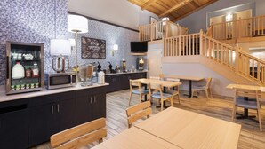 Une cuisine moderne avec des meubles de couleur sombre, un four à micro-ondes et une machine à café. Un escalier en bois mène à un niveau supérieur.