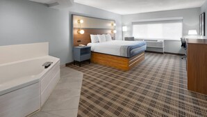 Une chambre d’hôtel avec un grand lit, une salle de bain séparée avec une baignoire, un bureau et une fenêtre avec des stores.