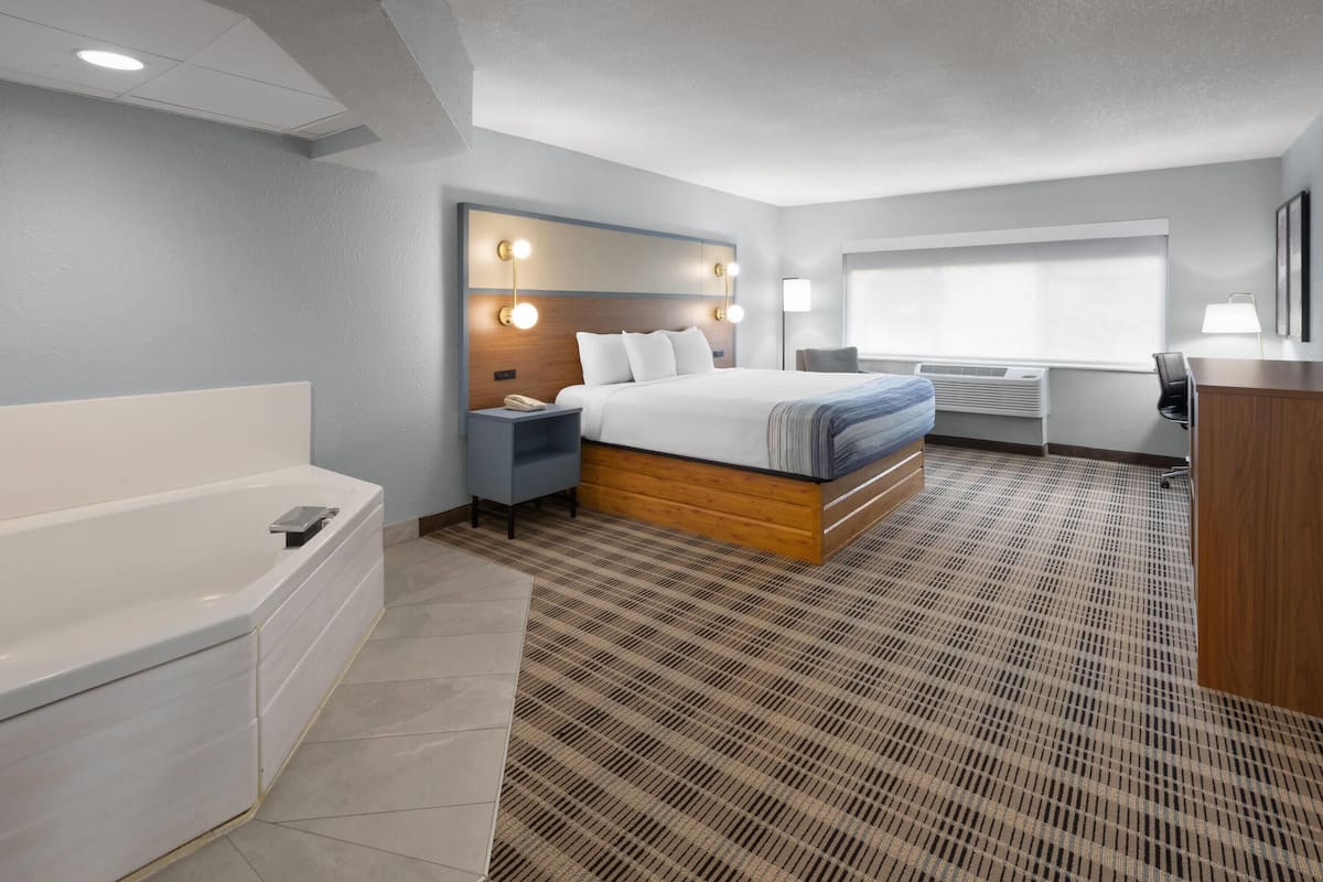 Une chambre d’hôtel avec un grand lit, une salle de bain séparée avec une baignoire, un bureau et une fenêtre avec des stores.