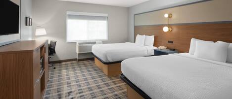 A hotel room with two beds, a desk, a chair, a TV, and a window with blinds.