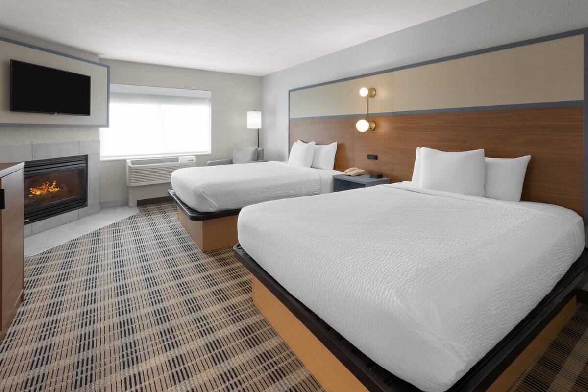 Une chambre d’hôtel avec deux lits, un téléviseur à écran plat, une cheminée et un grand miroir avec éclairage intégré.