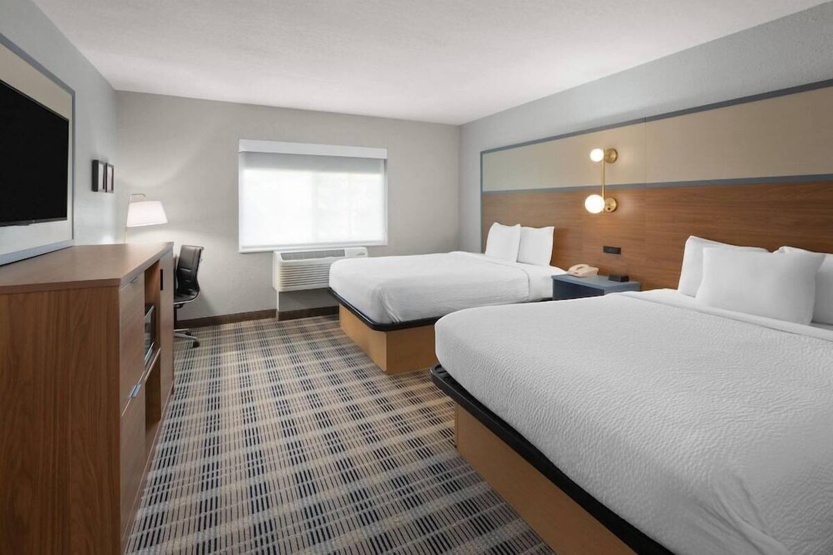Une chambre d’hôtel avec deux lits, un bureau, une chaise, une télévision, une lampe et une fenêtre.
