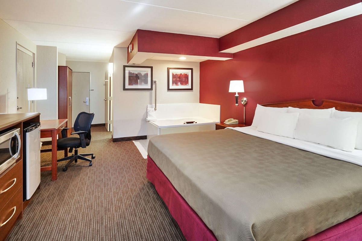 Une chambre d’hôtel comprenant un lit, un bureau, une chaise et une salle de bain avec baignoire.