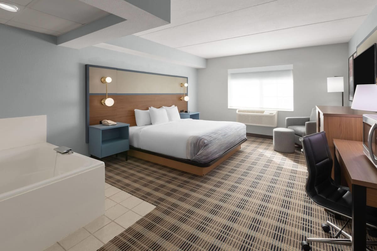 Une chambre d’hôtel moderne dotée d’un grand lit, de tables de chevet, d’un bureau, d’une chaise, d’une lampe de bureau, d’une télévision et d’une salle de bain avec baignoire.