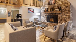 Un vaste espace de vie agrémenté d’une cheminée en pierre, de sièges confortables et d’un haut plafond avec balcon.