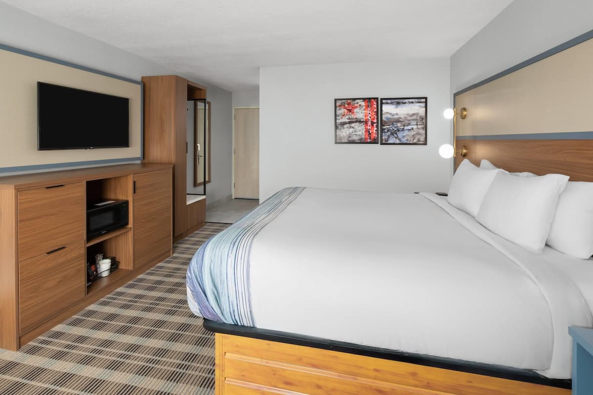 Une chambre d’hôtel avec un grand lit, une armoire en bois, un téléviseur à écran plat et deux tableaux encadrés au mur.