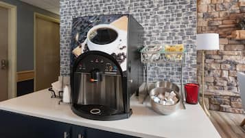 A coffee machine with a coffee cup design, a bowl of coffee beans, and a red cup on a kitchen counter.