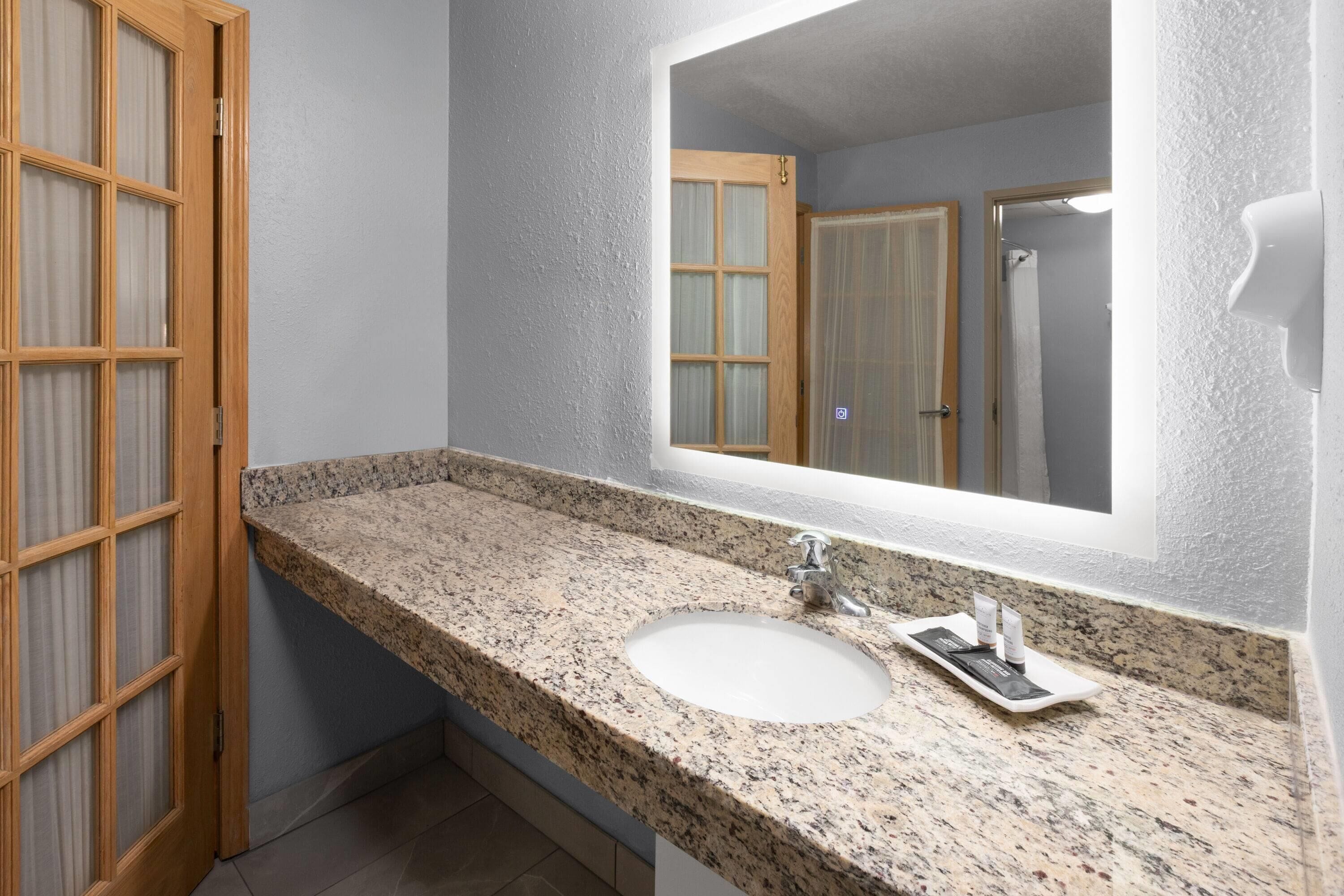 Un baño con lavamanos de encimera de granito, un espejo grande y una puerta de madera.