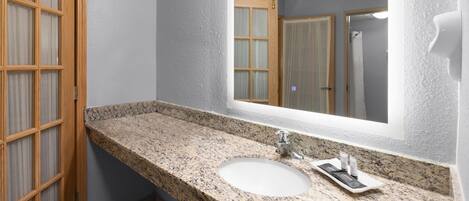 Un baño con lavamanos de encimera de granito, un espejo grande y una puerta de madera.