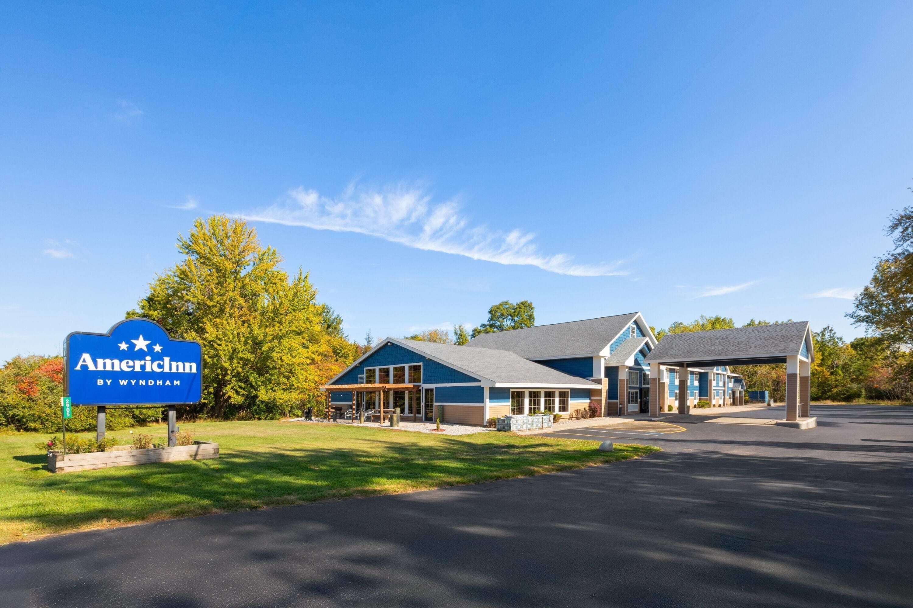 An American Inn by Wyndham with a blue and white exterior, a covered parking area, and a grassy lawn.