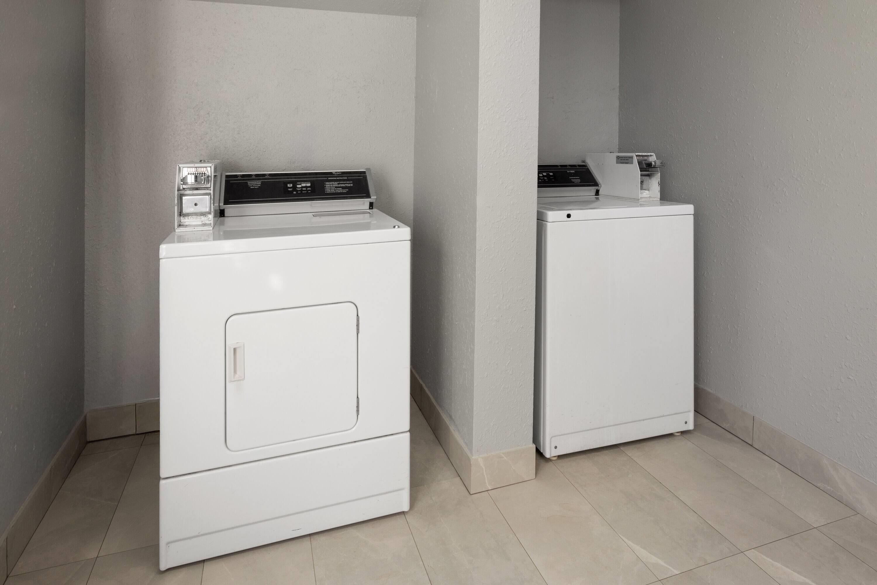 A laundry area with two stacked washers and dryers, a control panel, and a small light fixture.