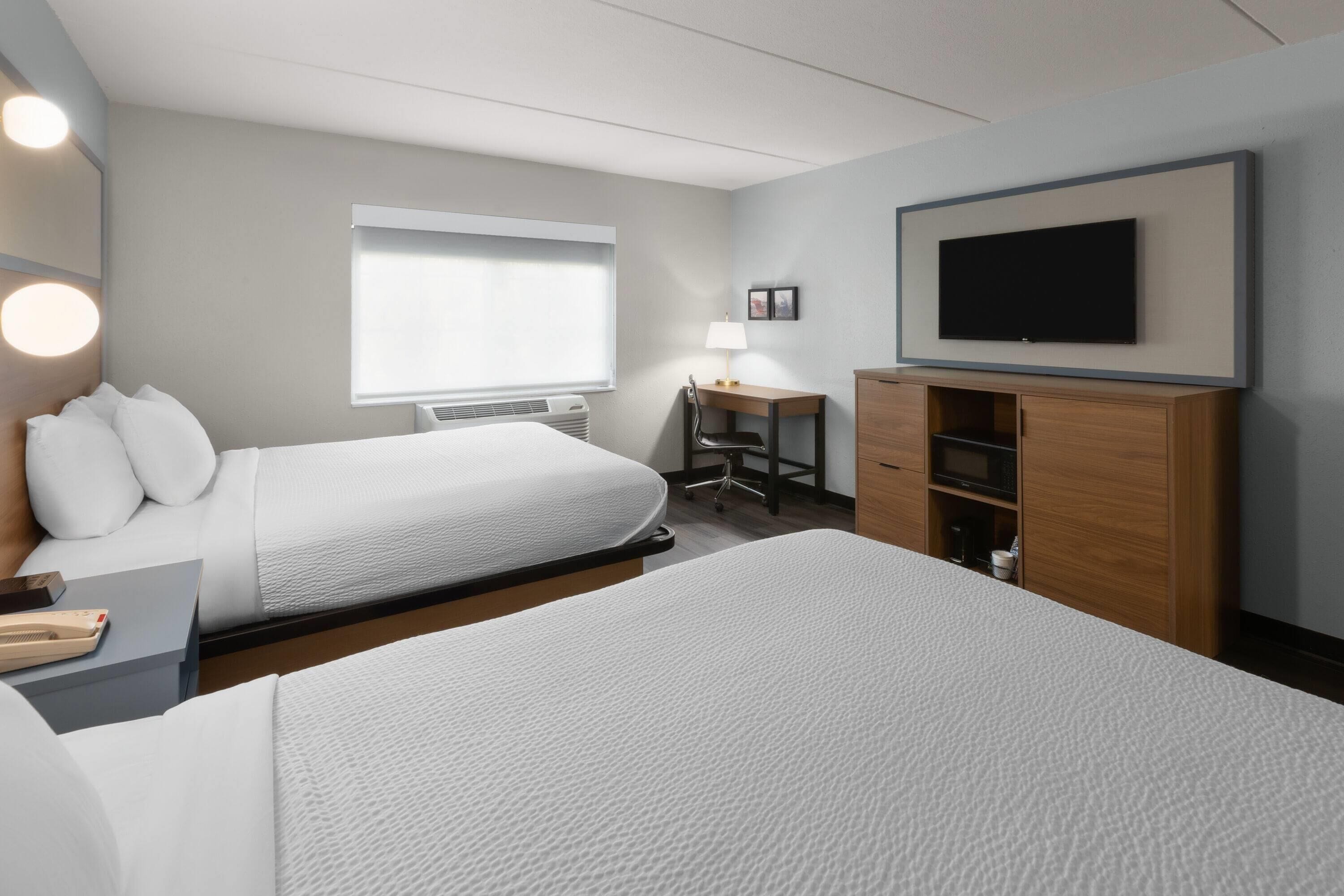 Una habitación de hotel con dos camas, un escritorio, un televisor y una ventana con persianas.
