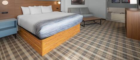 A hotel room with a large bed, a sofa, a desk, and a television.