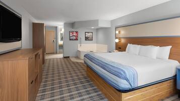 Quarto de hotel com uma cama grande, televisão, cómoda de madeira e casa de banho visível através de uma porta aberta.
