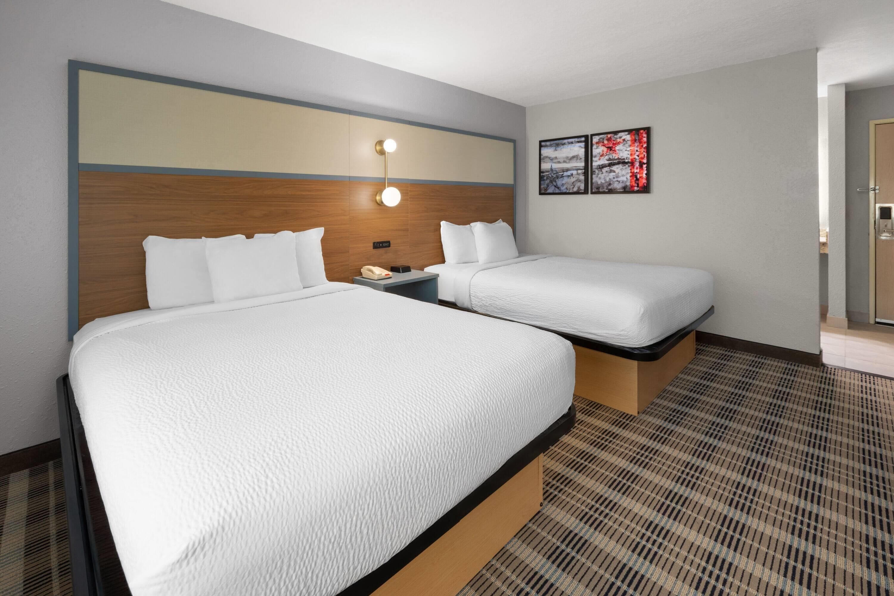 A hotel room with two beds, a wooden headboard, a nightstand with a phone, and a painting on the wall.