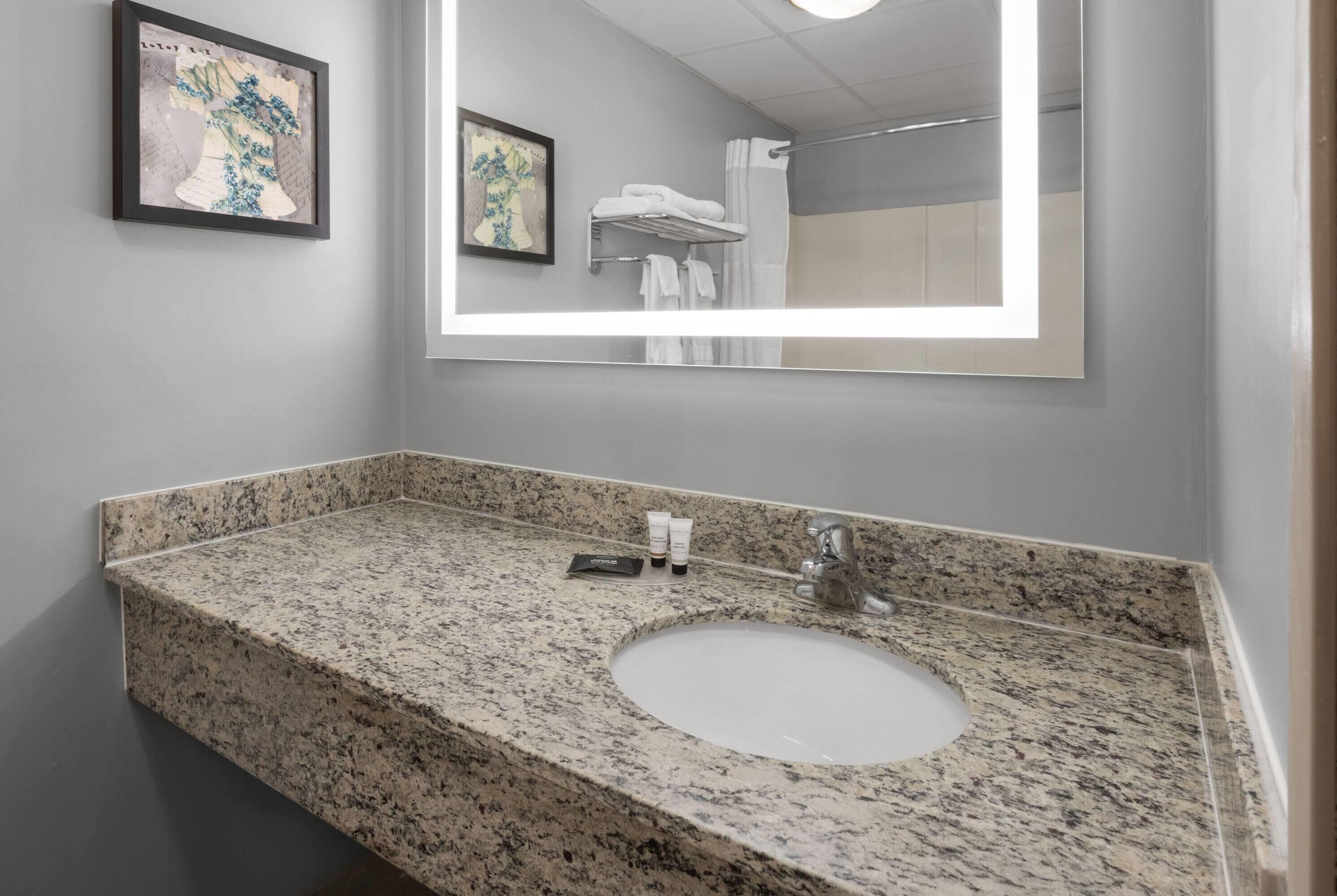 A bathroom with a granite countertop sink, a large mirror, and framed artwork on the wall.
