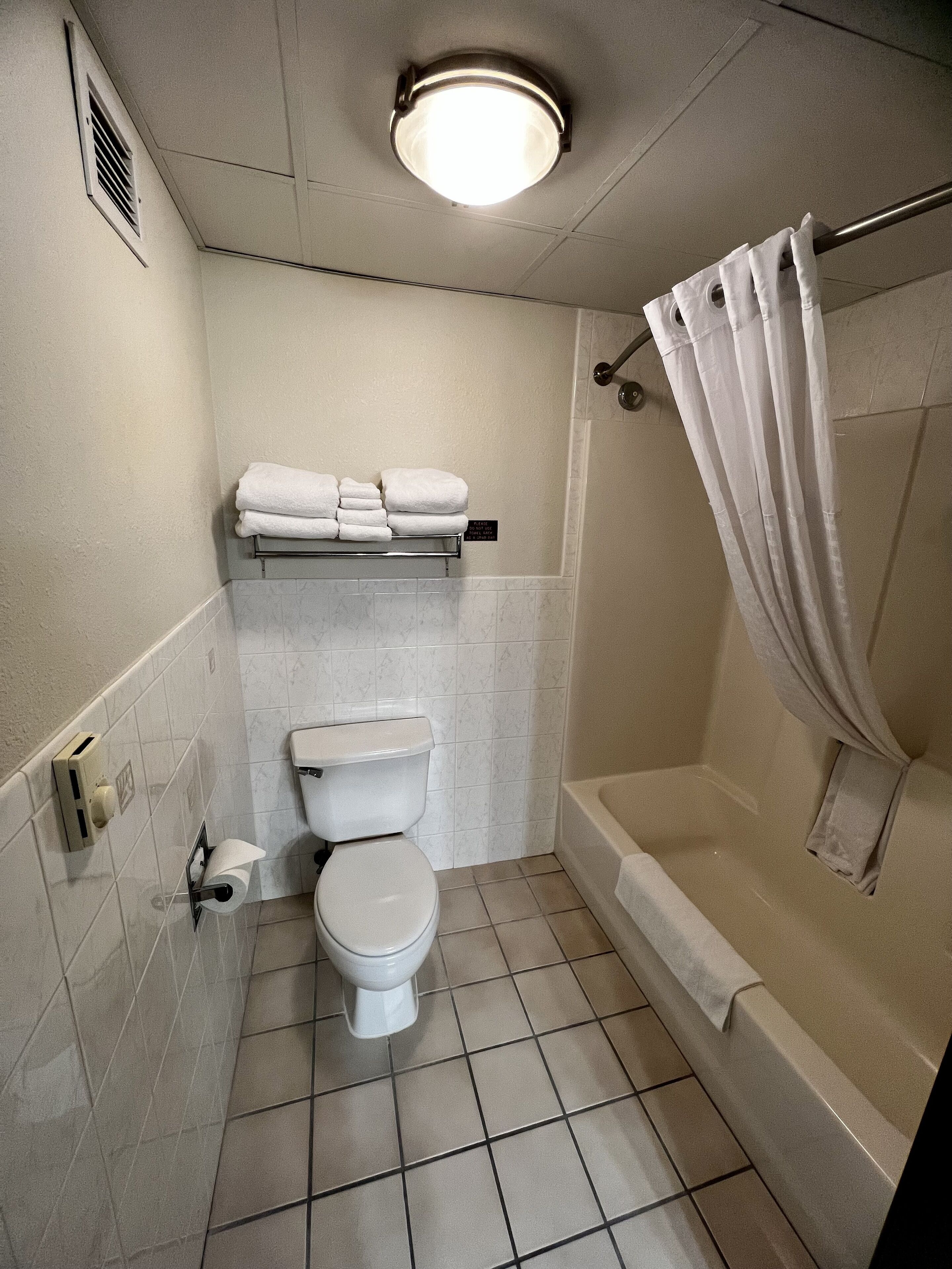 Een badkamer met een toilet, een plank met handdoeken, een douchegordijn en een plafondlamp.