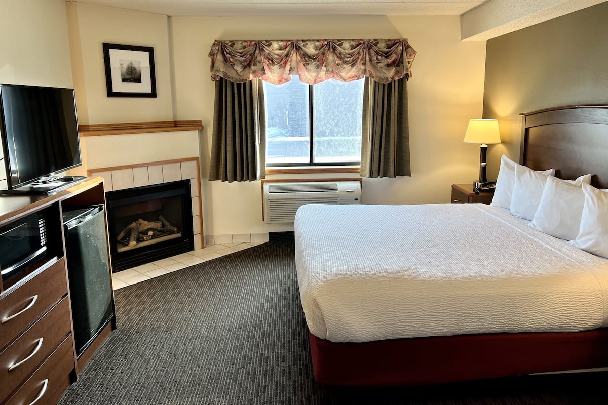 A hotel room with a bed, a television, a fireplace, and a window with curtains.