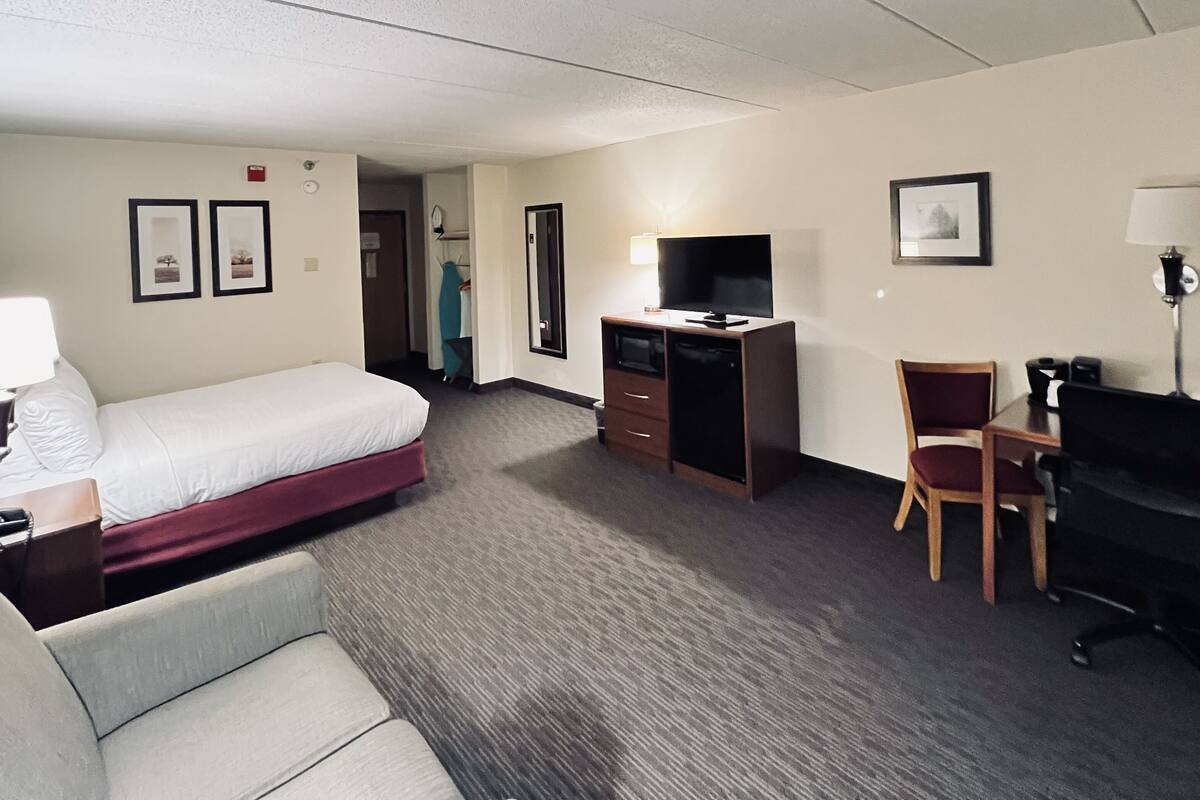 A hotel room with a bed, a desk with a computer, a chair, a TV, and a lamp.