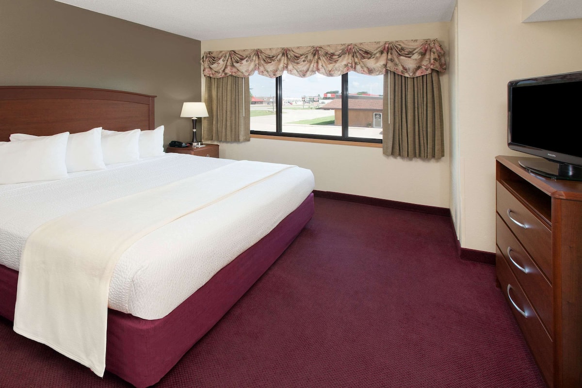 A hotel room with a large bed, a television, a nightstand, and a window with curtains.