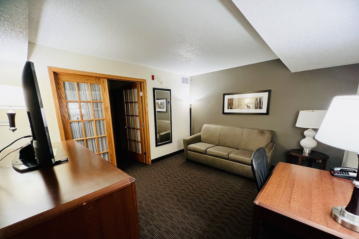 A hotel room with a desk, a sofa, a lamp, and a picture on the wall.