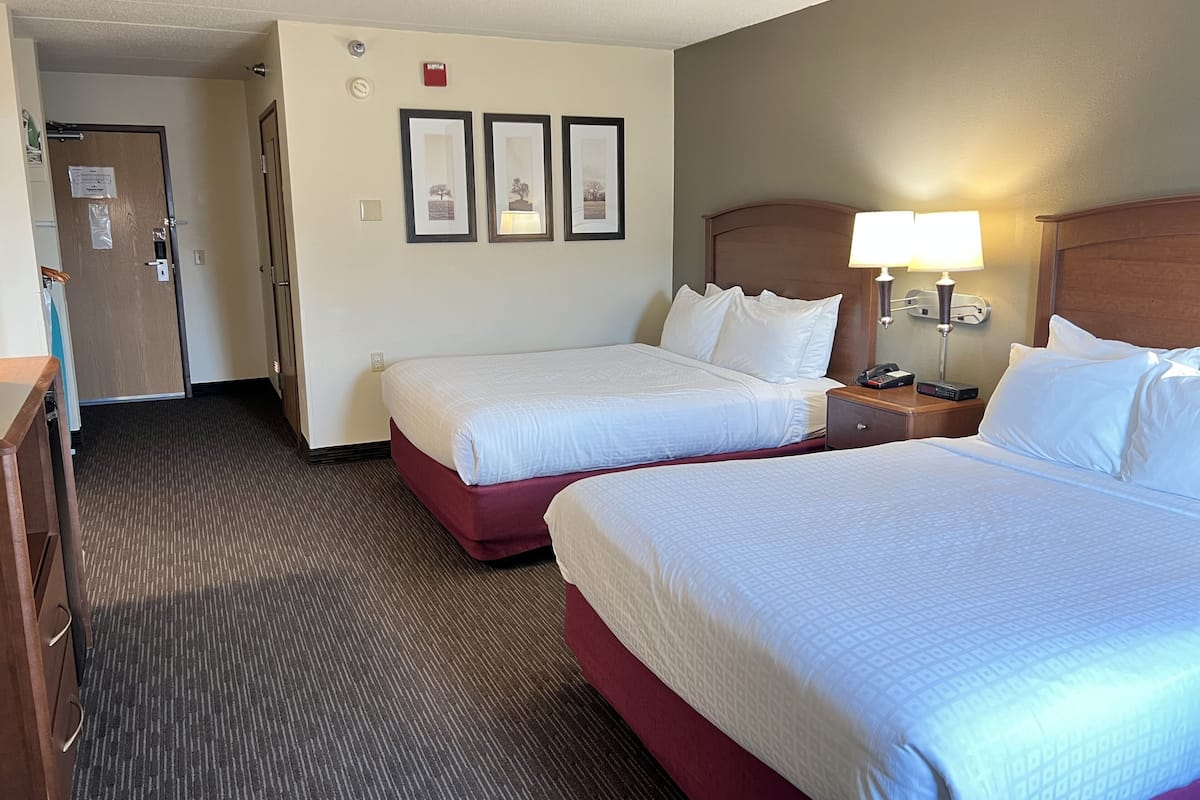 A hotel room with two beds, a desk, a chair, a lamp, and a door.