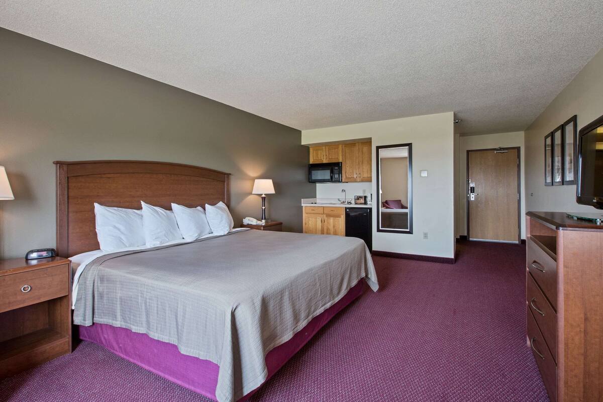 A hotel room with a large bed, a desk, a microwave, and a kitchenette.