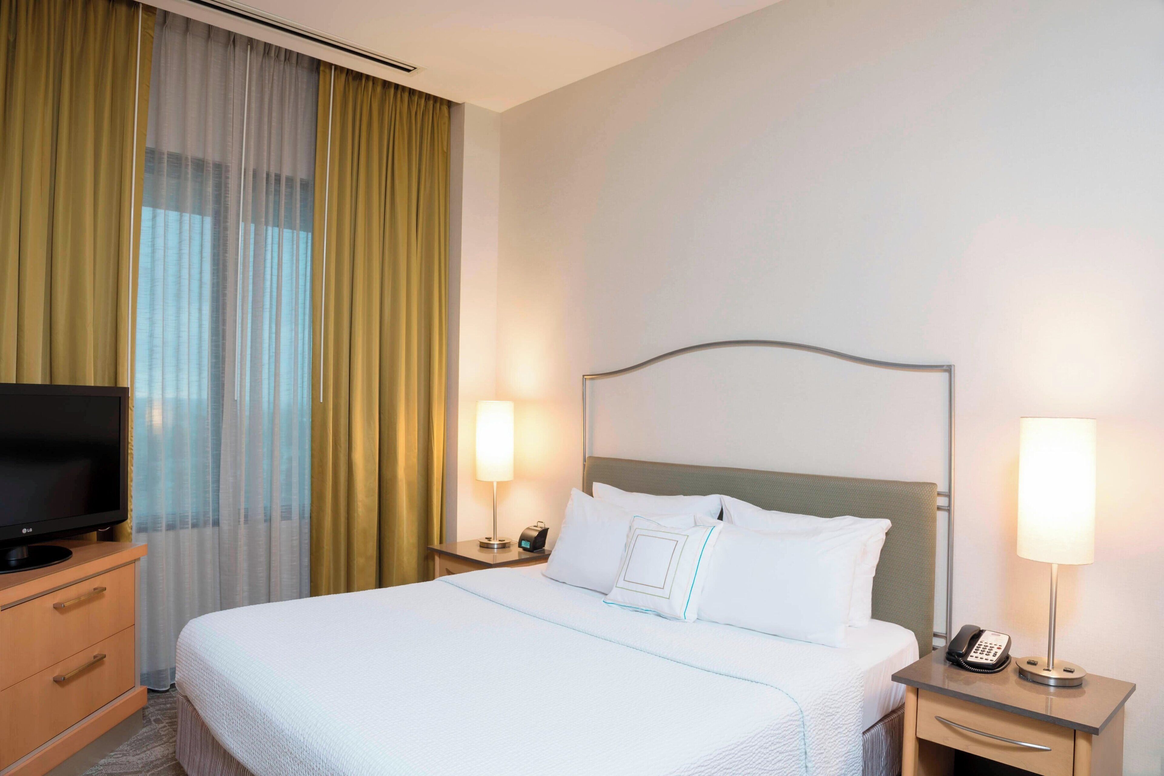 A hotel room with a bed, a TV on a dresser, two bedside lamps, and a telephone on the nightstand.