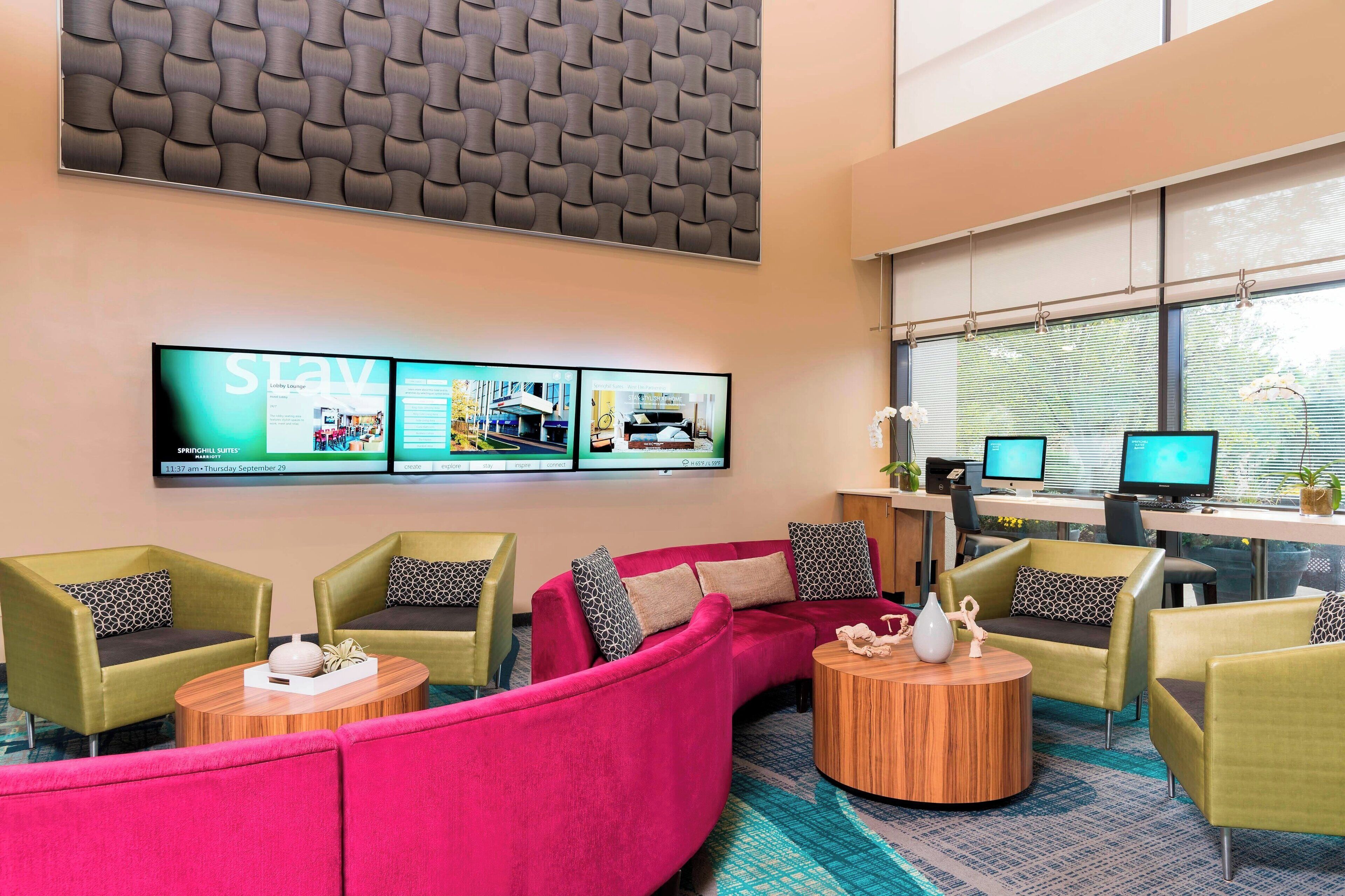 A modern lounge area with a curved sofa, armchairs, and a coffee table. There are multiple computer monitors and a large screen displaying information.
