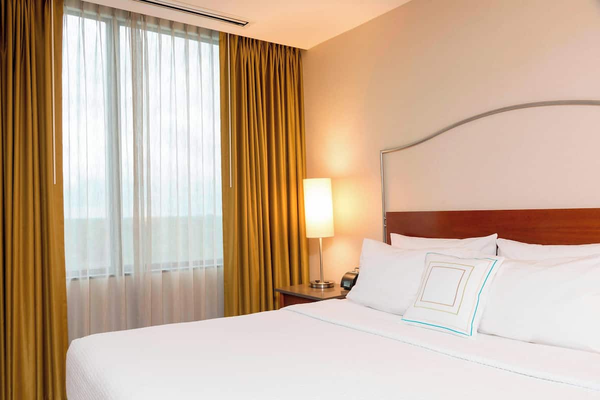A hotel room with a large bed, a bedside table with a lamp, and a window with curtains.