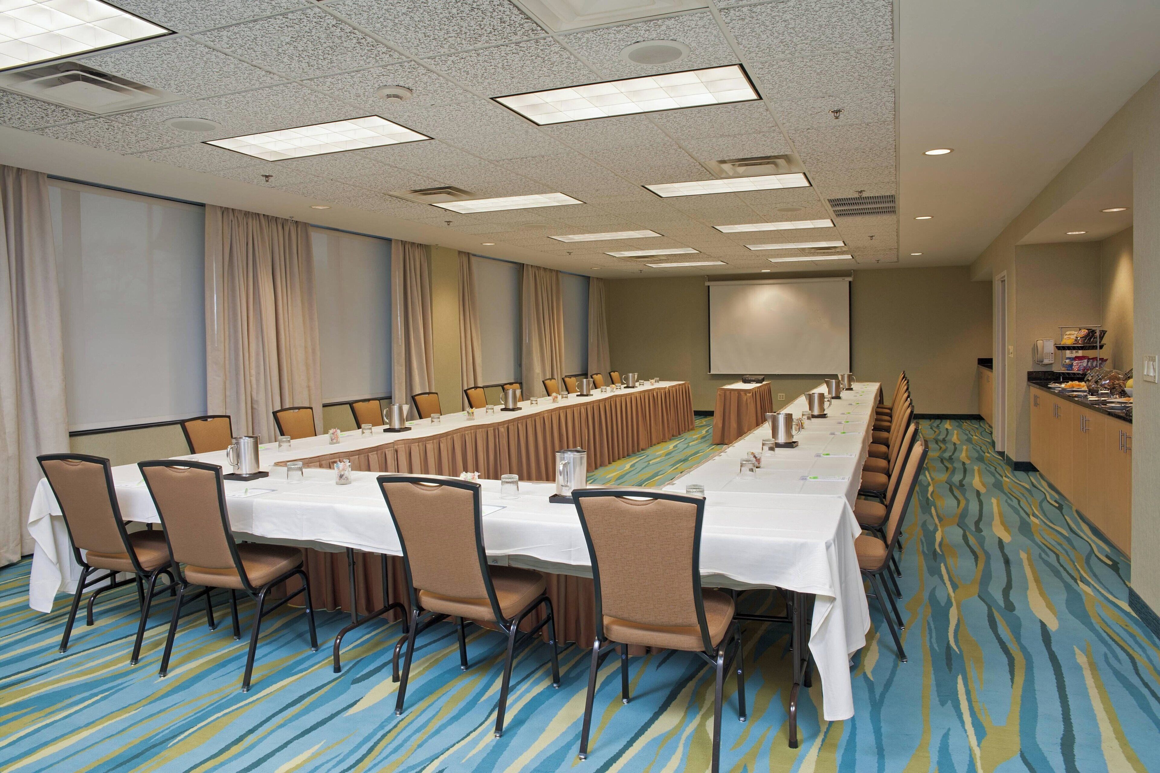A conference room with a long table, chairs, and a projector screen.