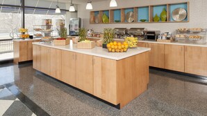 A modern kitchen with wooden cabinets, a central island with fruit, and a view of the outdoors. - SpringHill Suites Chicago O'Hare by Marriott (Chicago)
