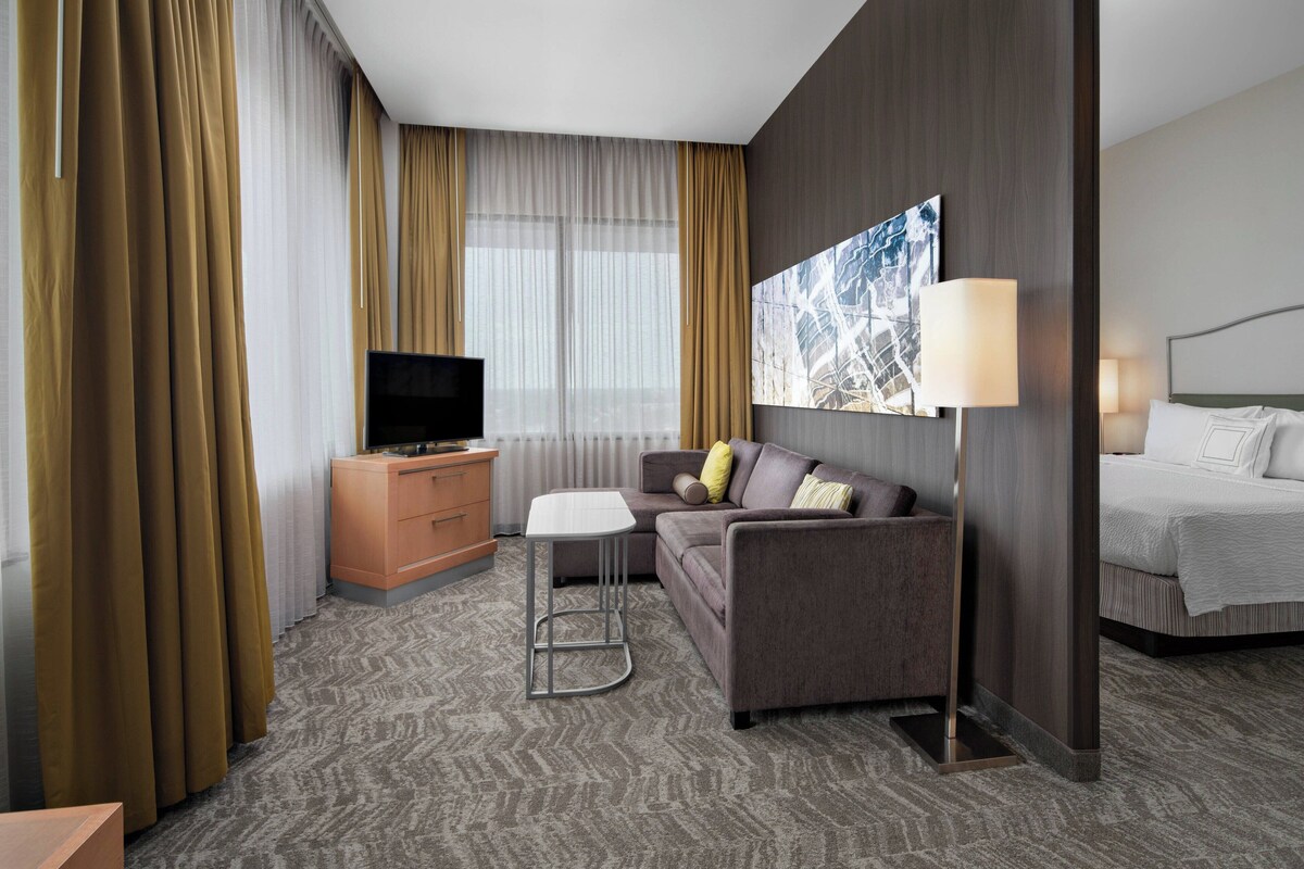 A hotel room with a sofa, a TV, a desk, a lamp, and a bed.