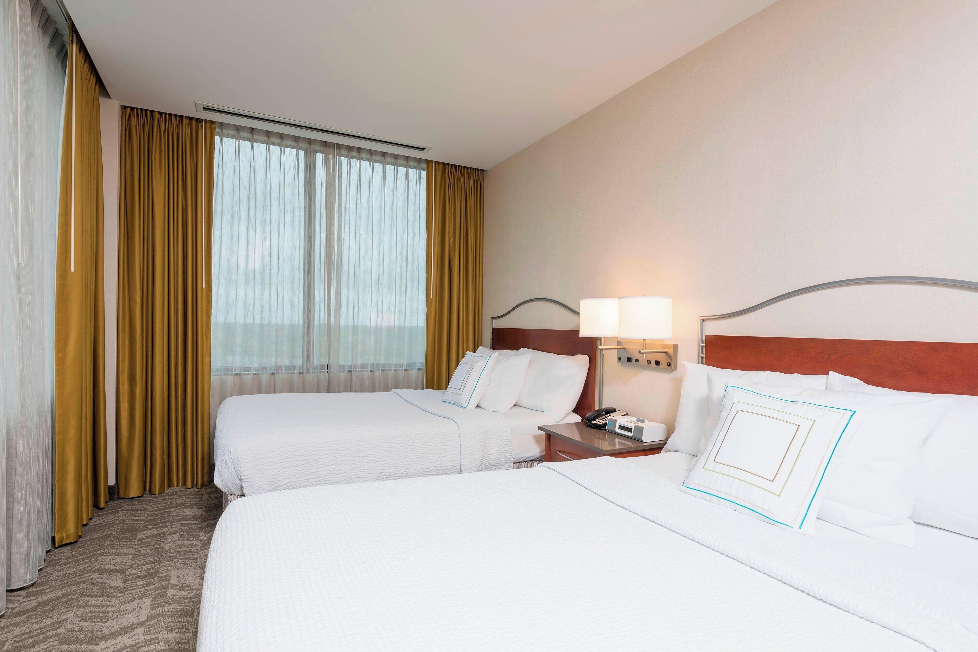 A hotel room with two beds, a nightstand with a lamp, and a window with curtains.